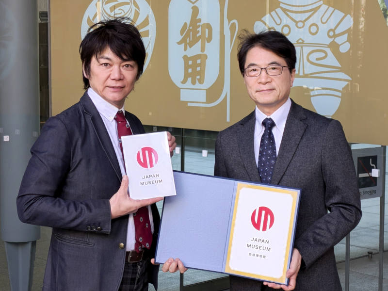 登録証とプレートを持つ石川幹人博物館長(情報コミュニケーション学部教授・右)と堀田秀吾副館長(法学部教授・左)